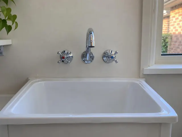Laundry sink with chrome tap set on a beige wall beside a window in Beecroft